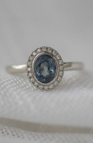 oval sapphire bezel set, with a halo of (20) bead-set diamonds in a polished 14K white gold band.